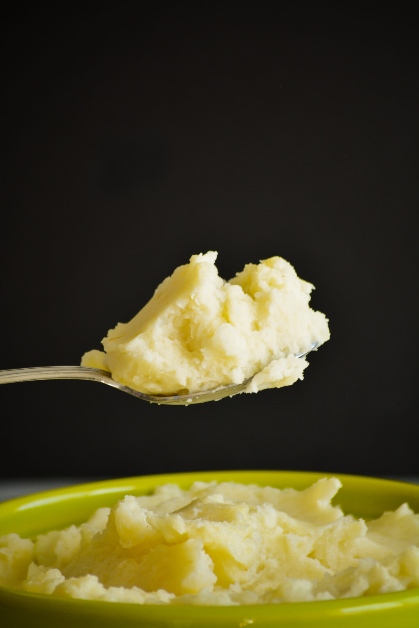 A spoonful of fluffy mashed potatoes held on top of a bowl of mashed potatoes.