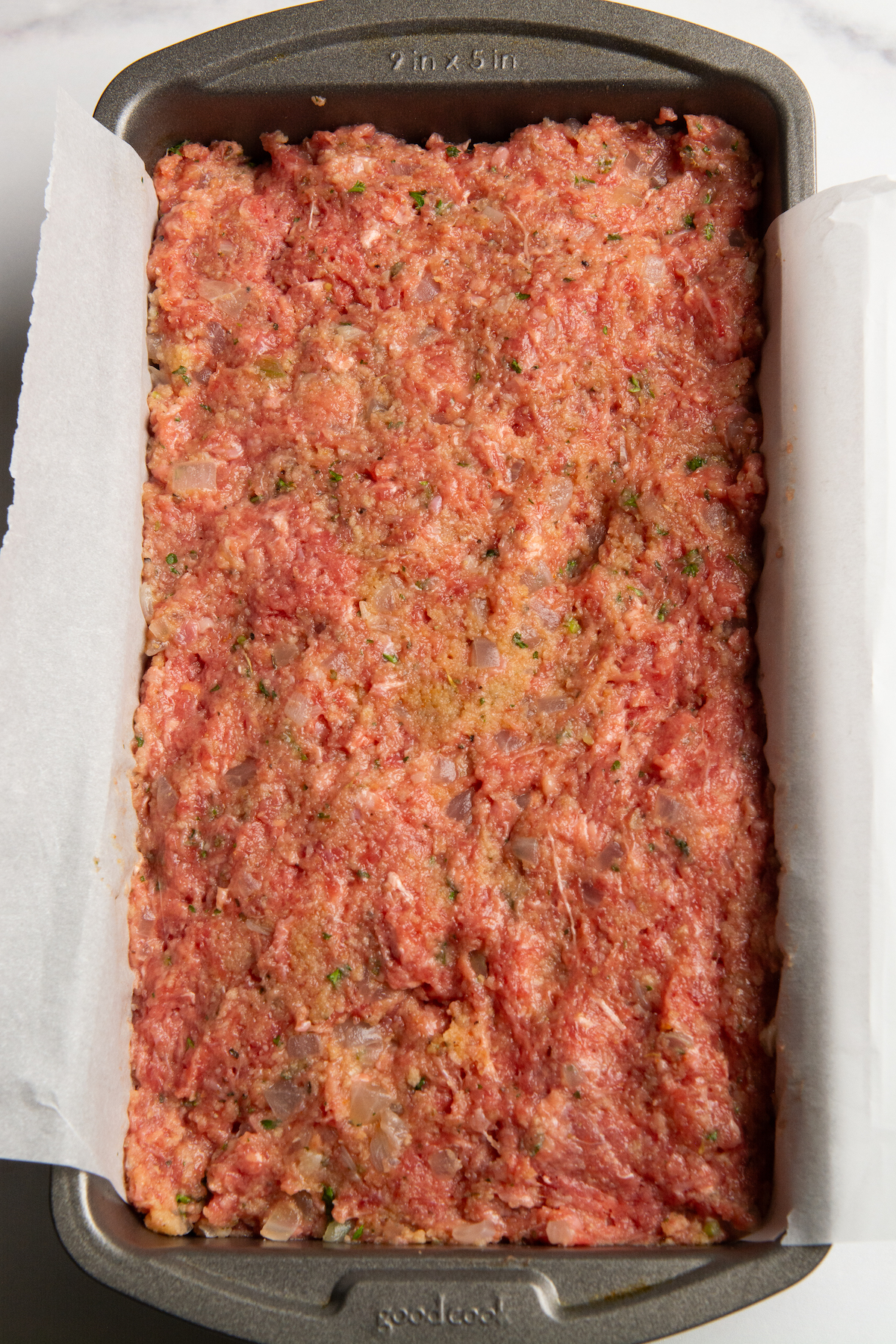 A loaf pan covered with parchment paper and filled with uncooked meatloaf