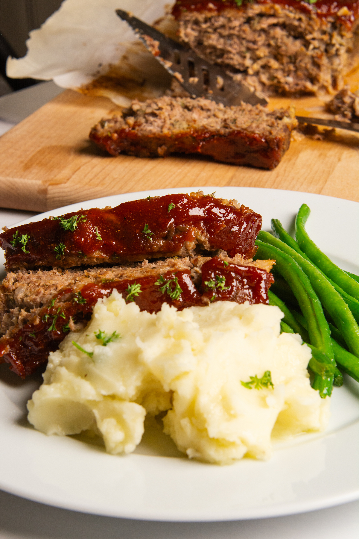 A plate with meatloaf and a sweet glaze, with green beans and mashed potatoes