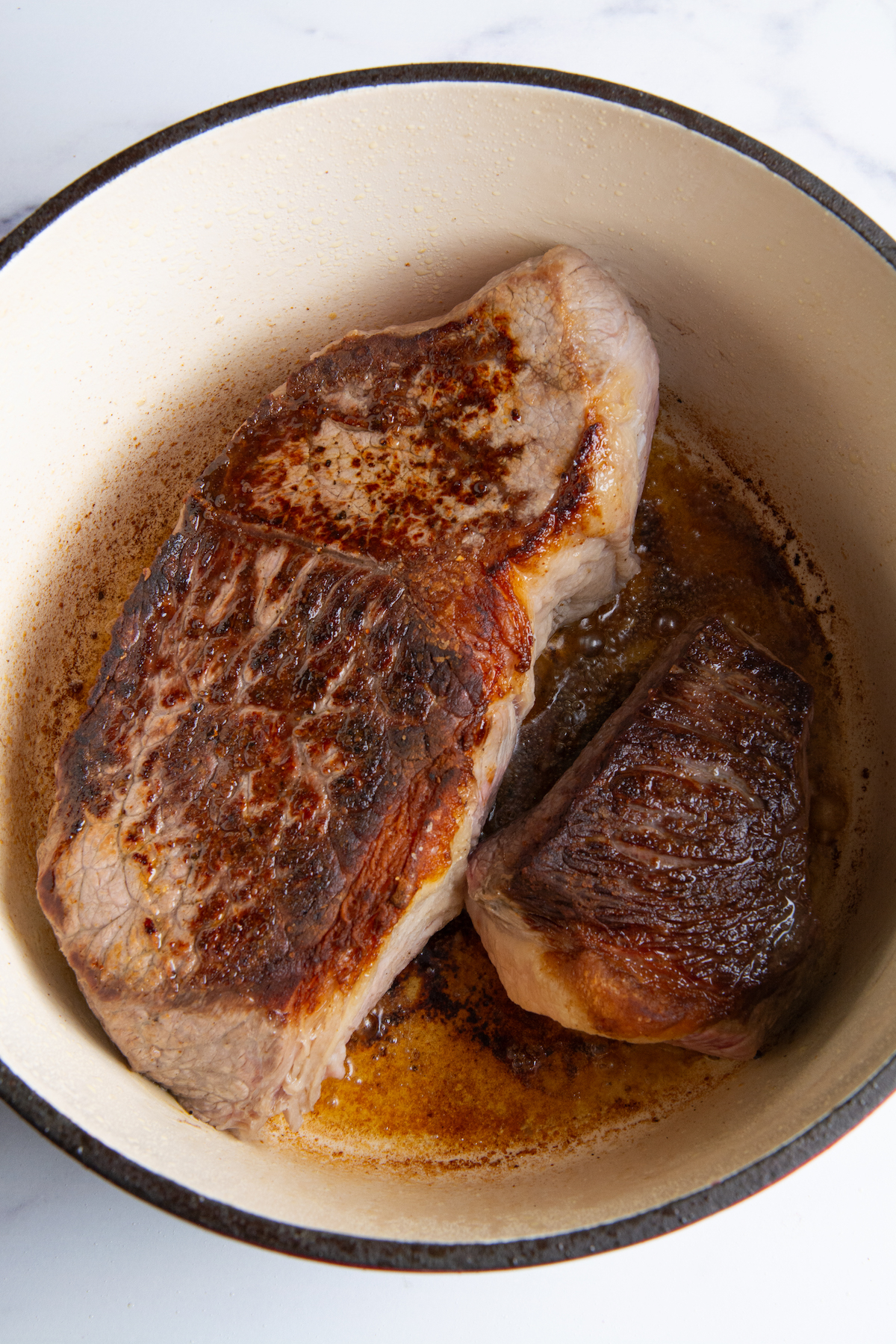 A large Dutch oven with round roast beef seared on both sides.