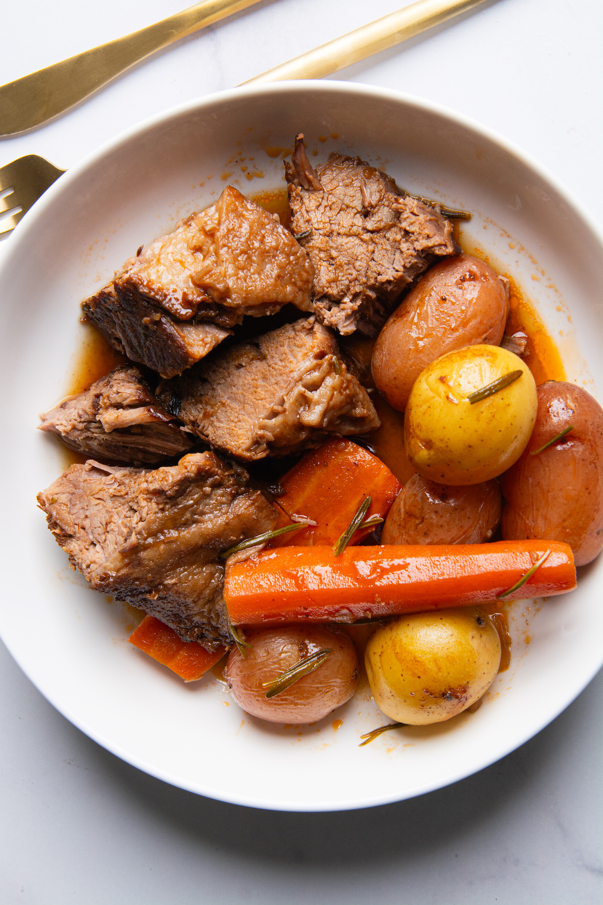 A plate with chunks of juicy pot roast with roasted baby potatoes and carrots.