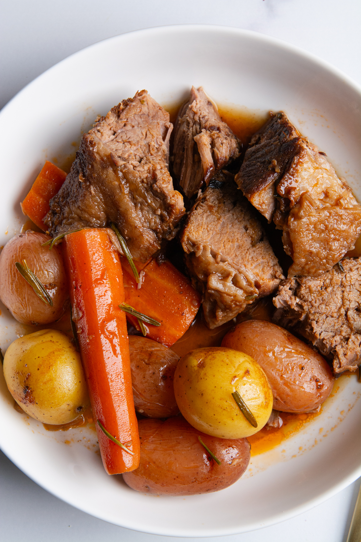 A plate with chunks of juicy pot roast with roasted baby potatoes and carrots.