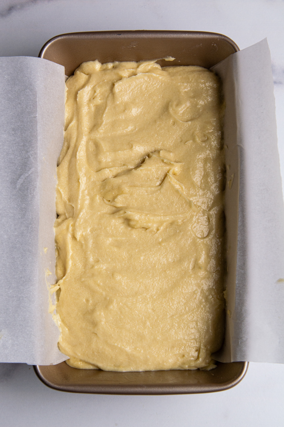 Raw pound cake batter in a loaf pan covered with parchment paper.