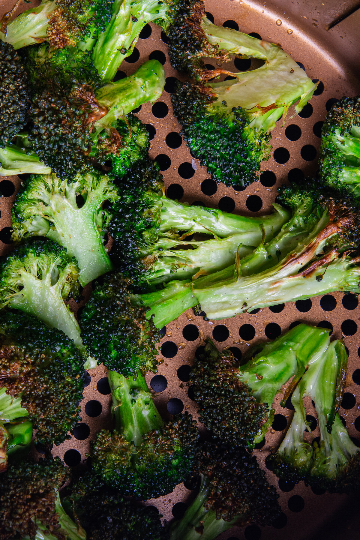 An air fryer basket with roasted broccoli florets.