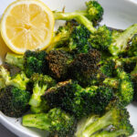 A plate with roasted broccoli florets with half a lemon resting on the side.