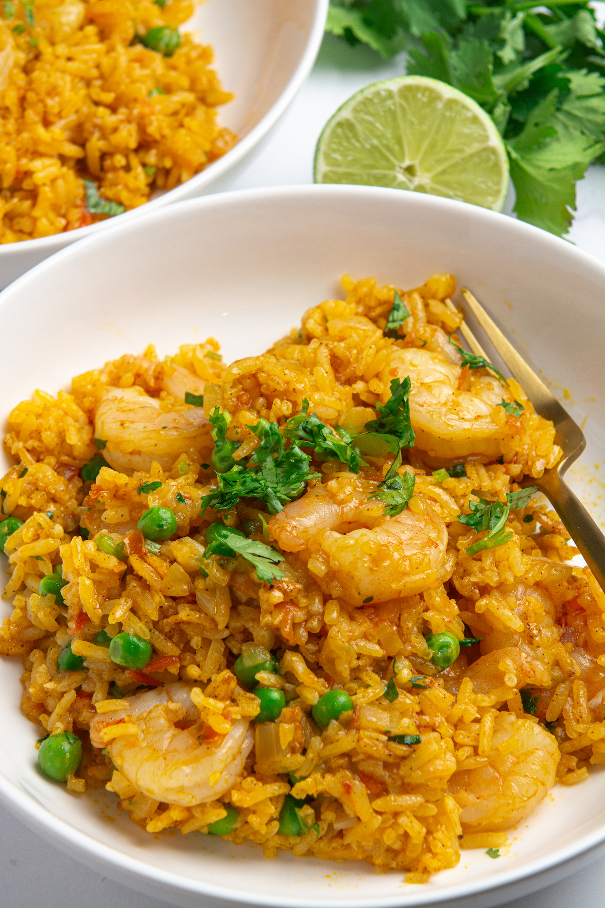 A dish with arroz con camarones or shrimp and rice, peas, and cilantro with a fork on the side.