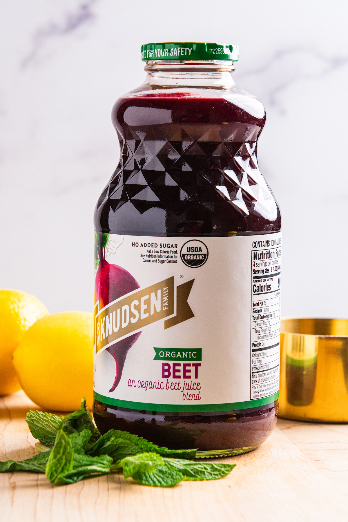 A bottle of beet juice, with lemons and mint around it.