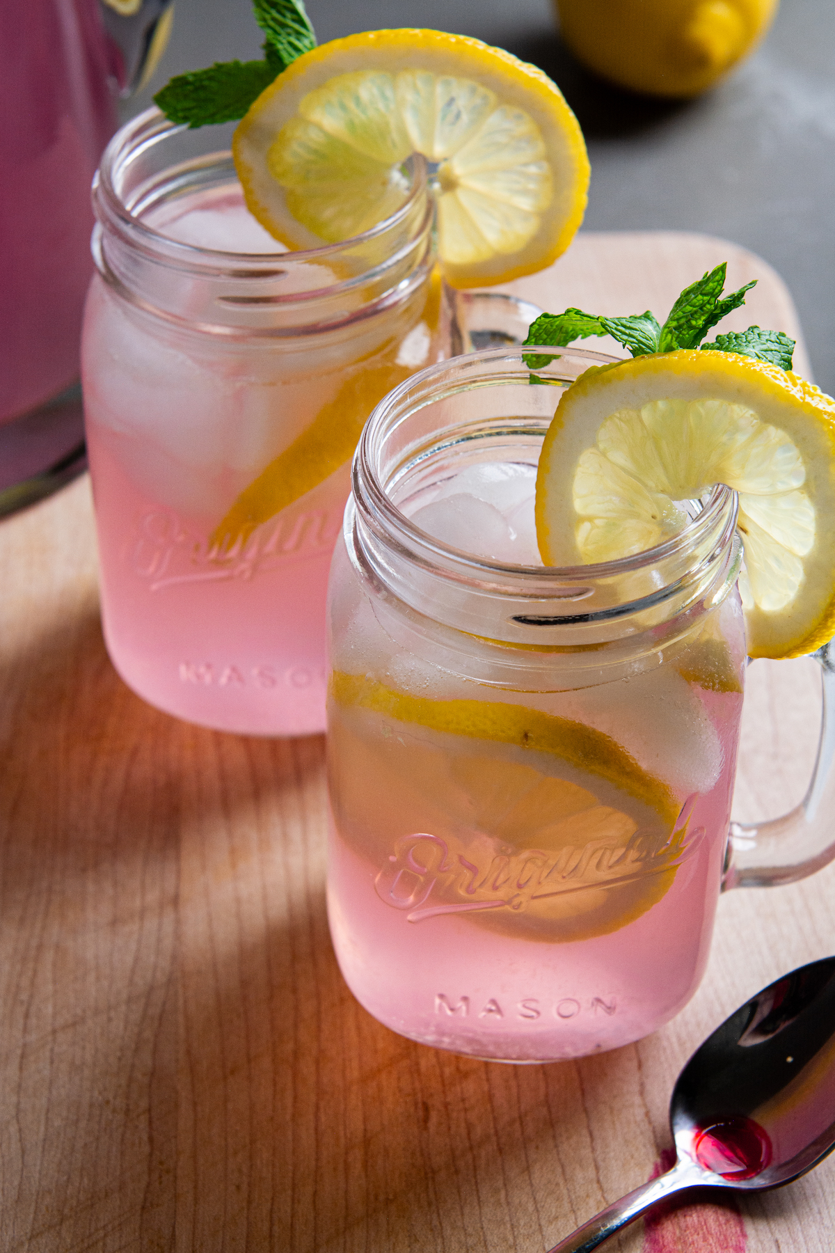 Two glasses of pink lemonade with lemon slices and mint leaves.