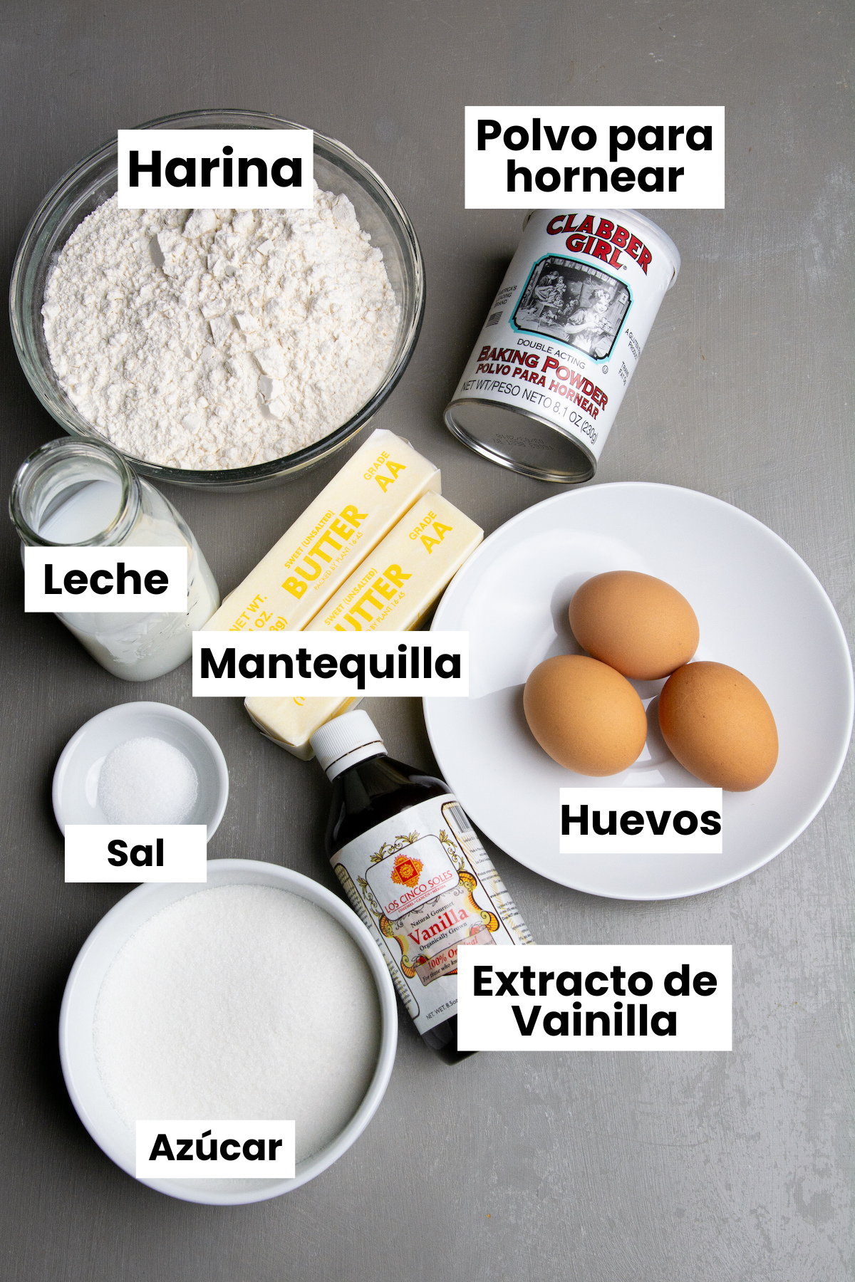 Ingredients for making pound cake, flour, baking powder, milk, butter, salt, huevos, sugar, vanilla extract labeled in Spanish.
