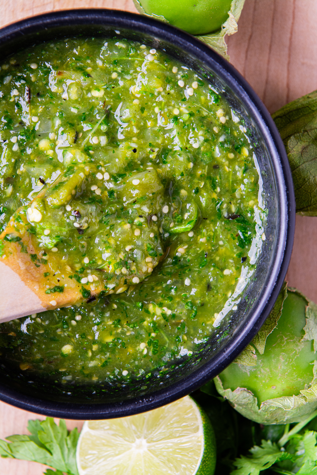 A bowl of roasted tomatillo salsa verde with half a lime and a tomatillo around it.
