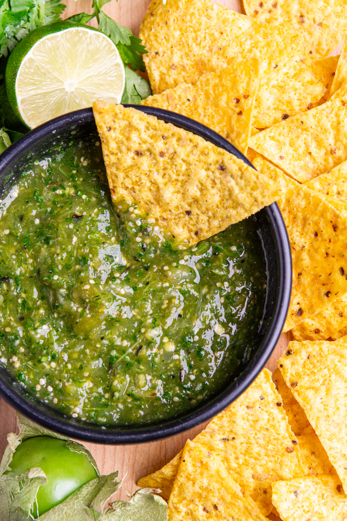 A bowl of Roasted Tomatillo Salsa Verde with half a lime, corn chips and a tomatillo around it.