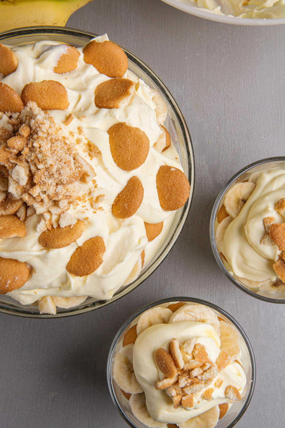 A large bowl and two small glasses filled with banana pudding, topped with Nilla wafer.