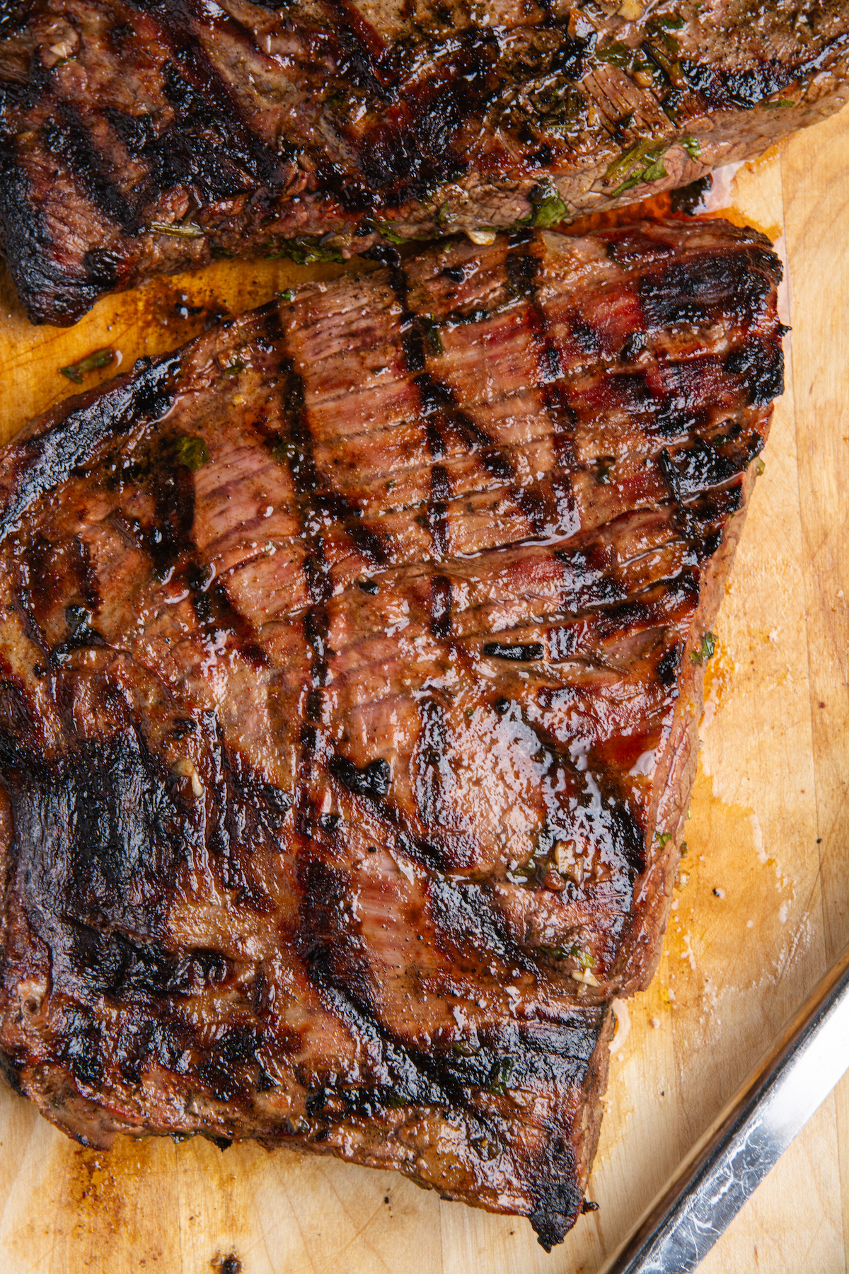 A large portion of grilled flank steak or carne asada resting on a wooden cutting board.