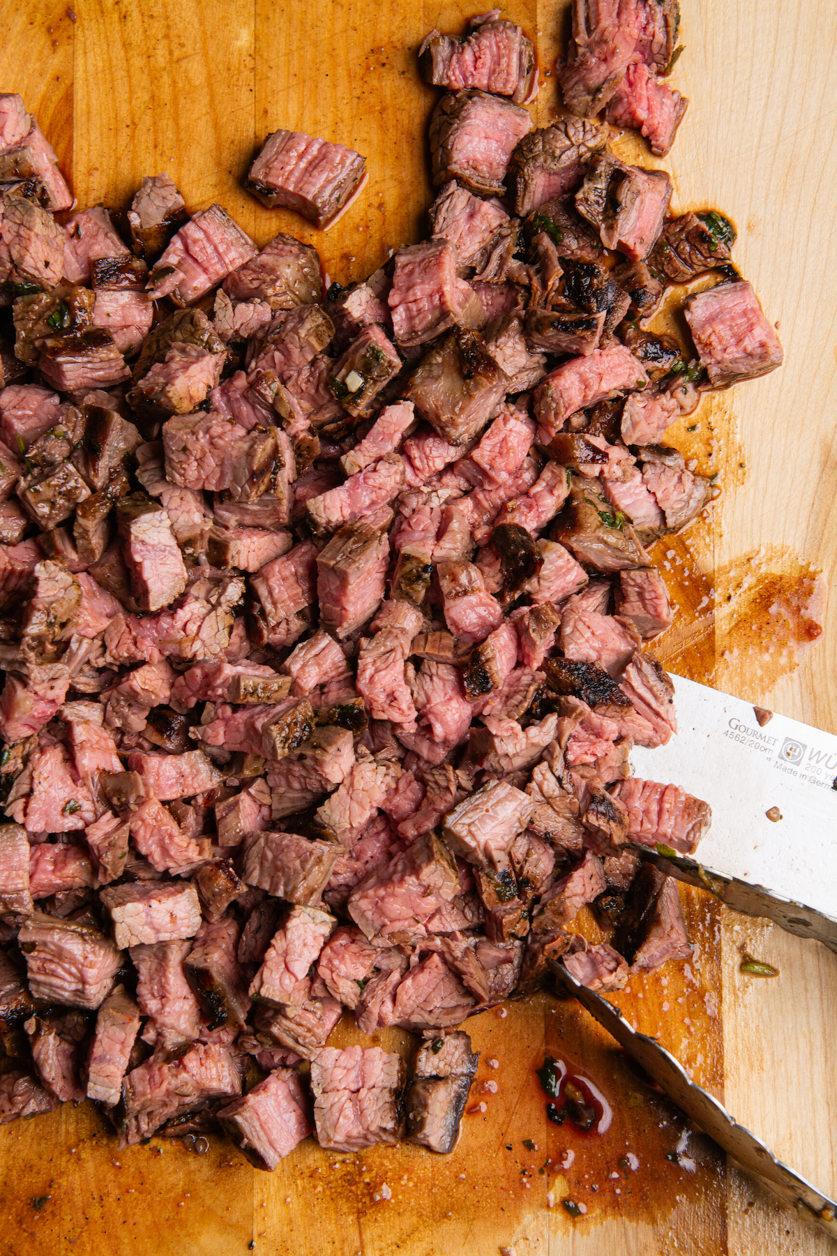 Grilled flank steak or carne asada chopped into smaller pieces on a wooden cutting board.