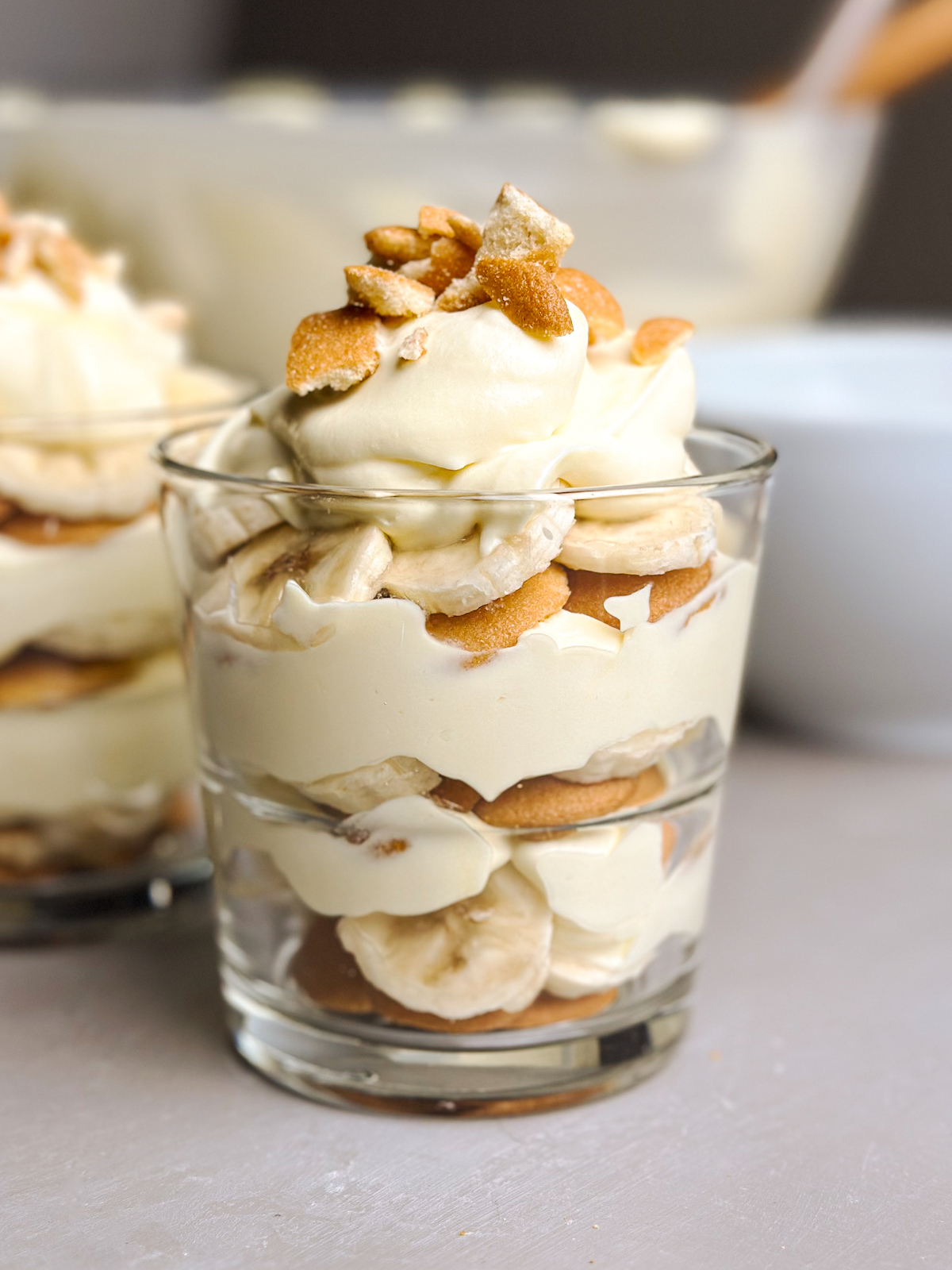 A glass of banana pudding with three layers of Nilla wafers, sliced bananas, vanilla pudding, topped with crumbles of Nilla wafers.