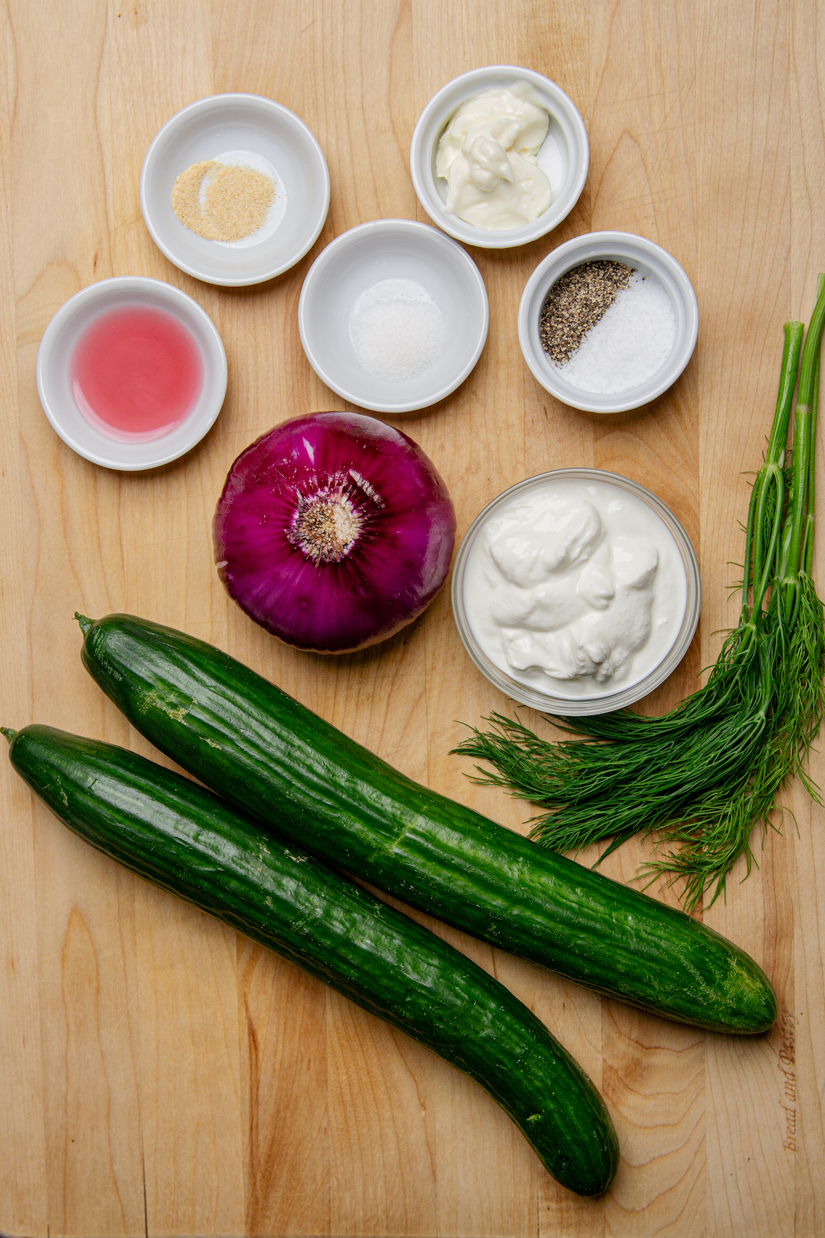 Ingredients for a creamy cucumber salad, which include, English cucumbers, red onion, red wine vinegar, fresh dill, garlic powder, white sugar, salt, and pepper.