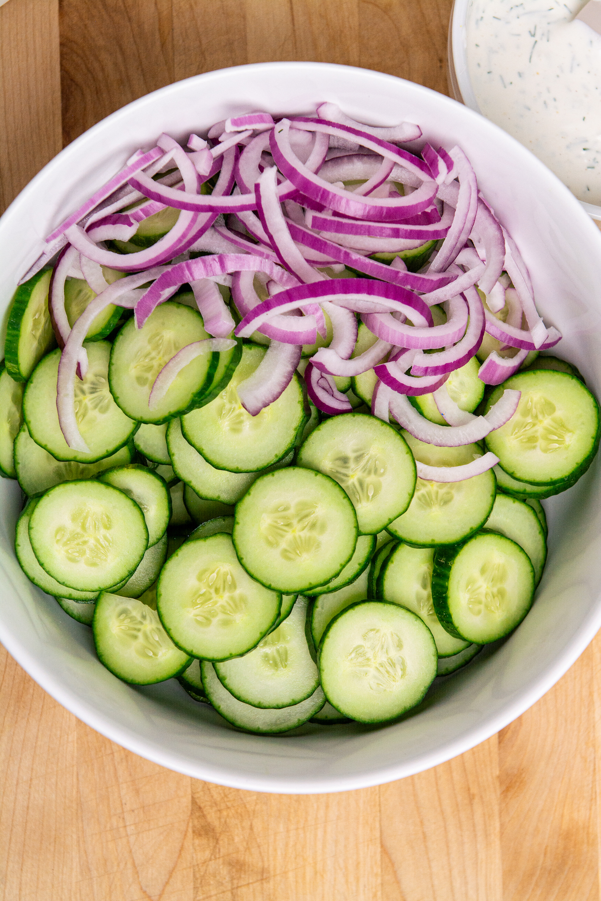 A large salad bowl with sliced English cucumbers and sliced red onion.