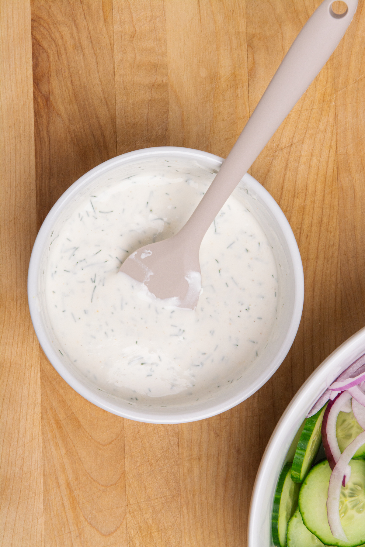 A small bowl of sour cream dressing for a creamy cucumber salad.