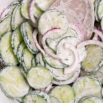 A bowl of sliced English cucumbers and sliced red onion tossed in a sour cream dressing.