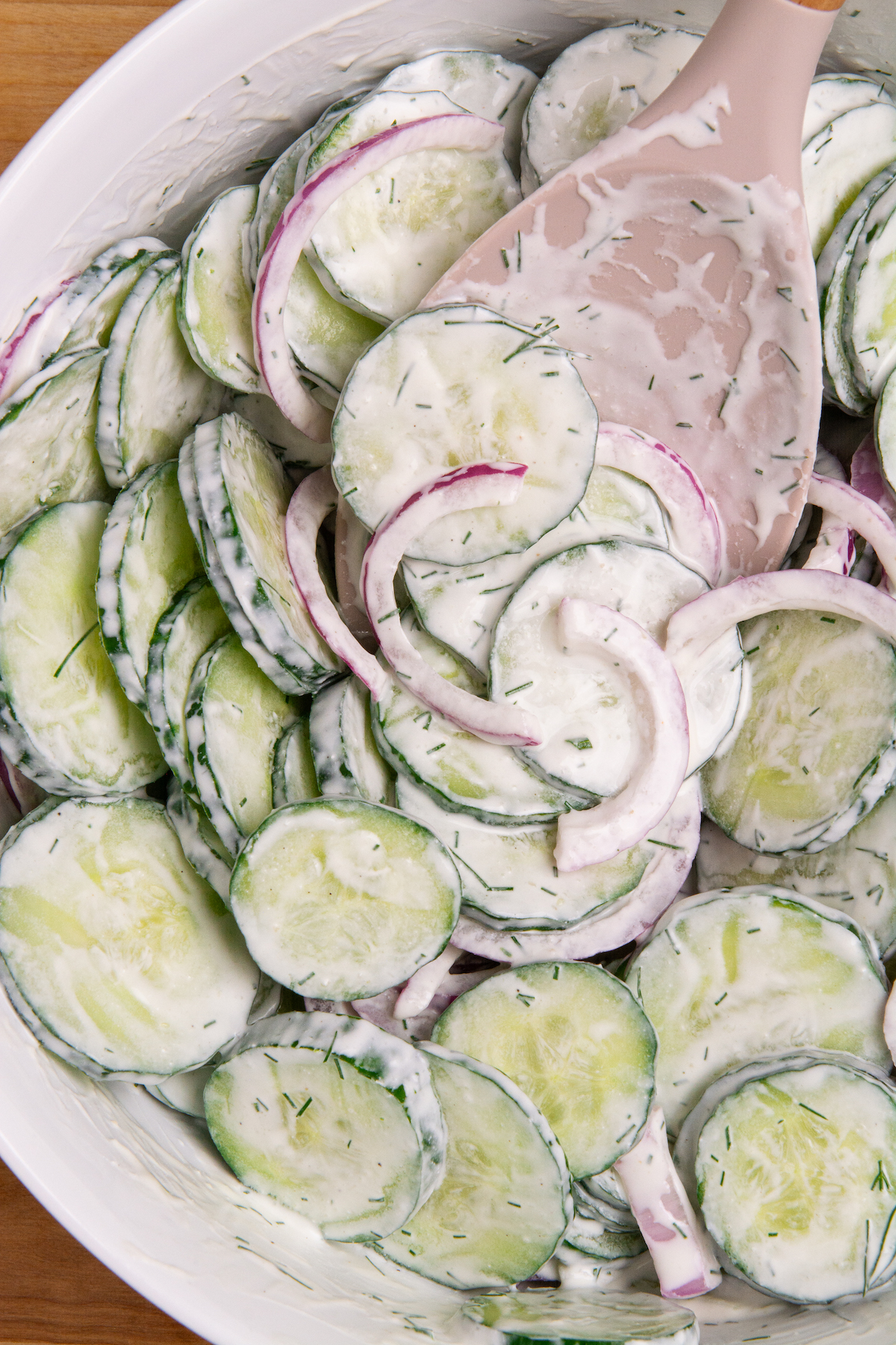 A bowl of sliced English cucumbers and sliced red onion tossed in a sour cream dressing.