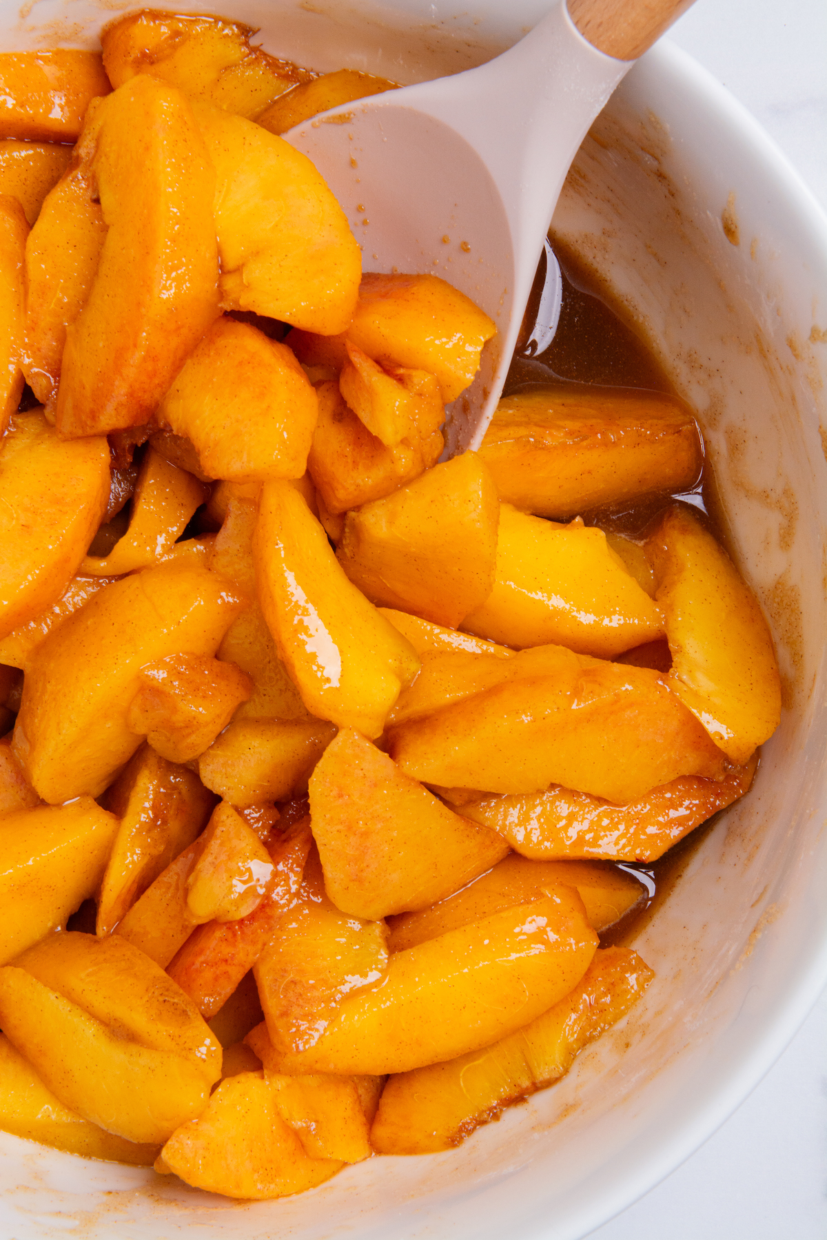 A bowl of sliced peaches coated with peach cobbler filling.