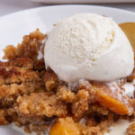 A serving of peach cobbler topped with a scoop of vanilla ice cream.