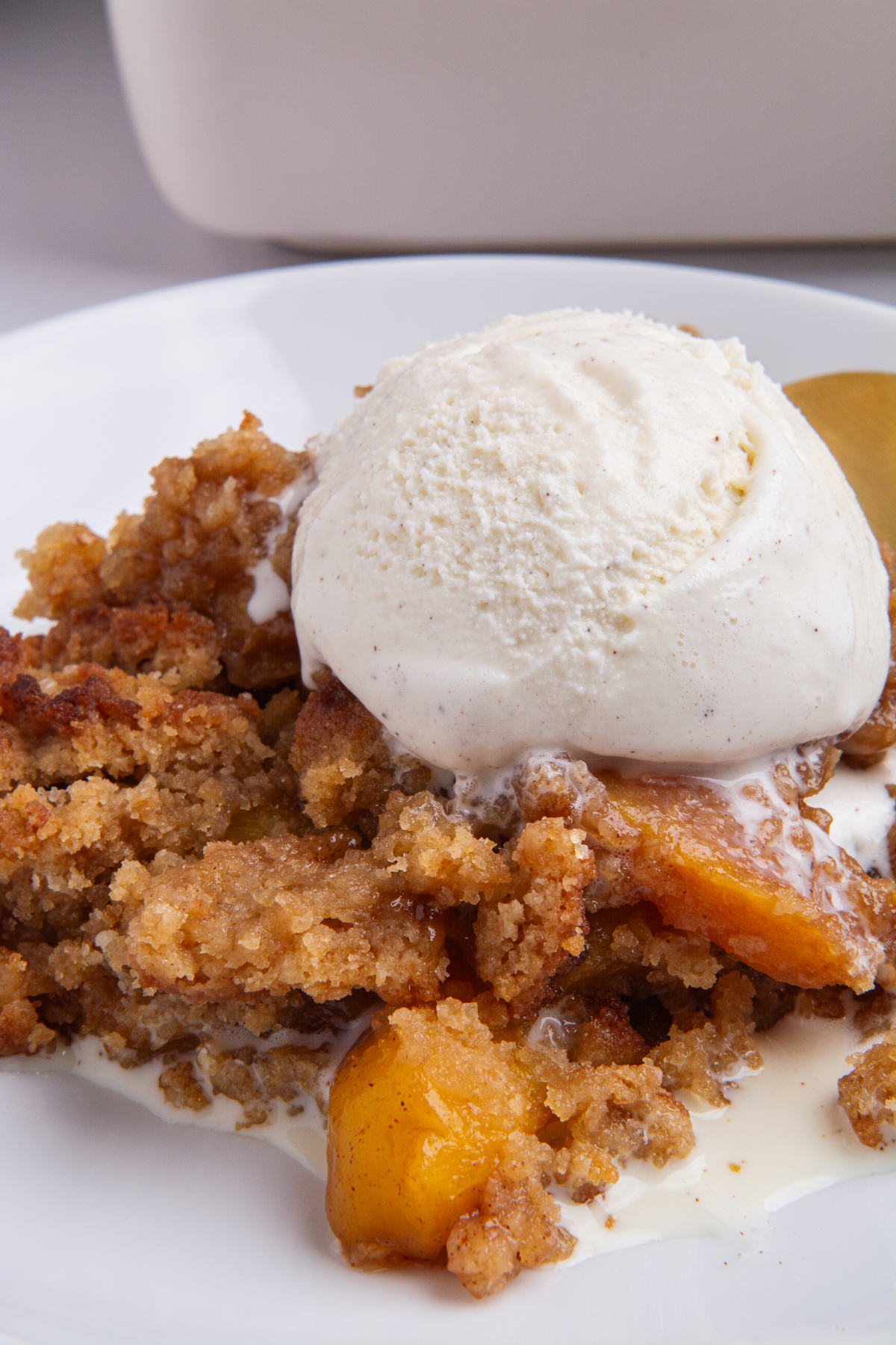 A serving of peach cobbler topped with a scoop of vanilla ice cream.