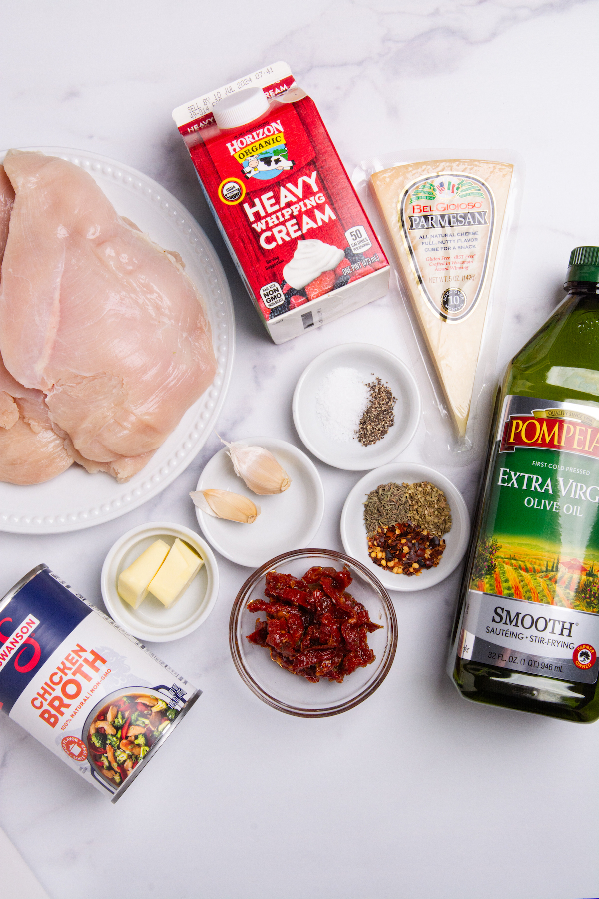 Ingredients for Marry Me Chicken, chicken breasts, heavy cream, chicken stock, olive oil, butter, Parmesan cheese, garlic, thyme, oregano, chili flakes, and sun-dried tomatoes.