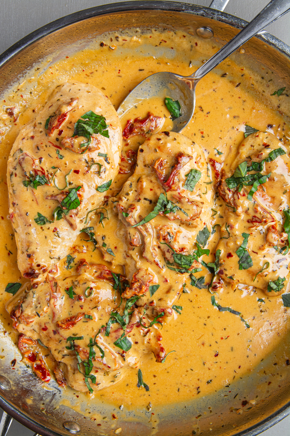 A large skillet with sautéed chicken breasts garnished with chopped basil in a Marry Me Chicken sauce made with chicken stock, heavy cream, parmesan, spices and sun-dried tomatoes.