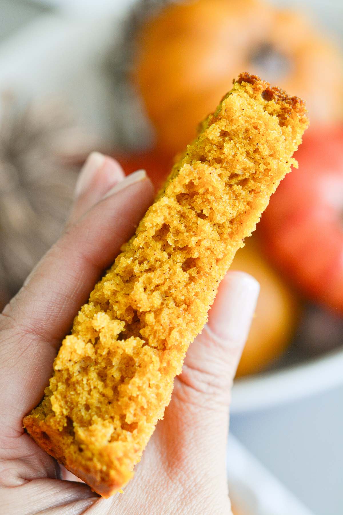 A hand holding a fluffy slice of pumpkin bread.