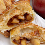 A baked and golden brown apple turnover cut in half showing a delicious caramel apple filling.