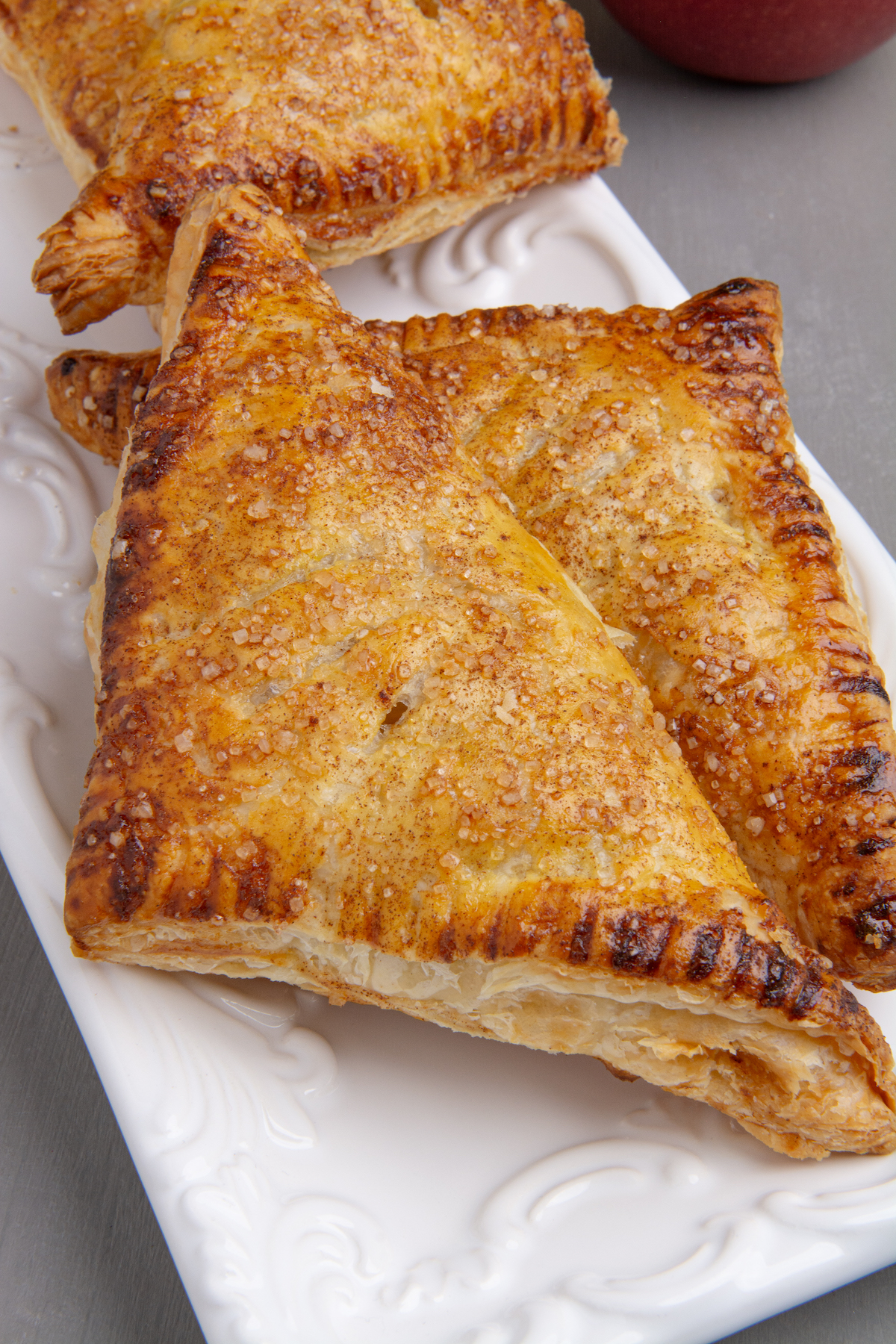 Two baked golden brown apple turnovers on a white serving dish.