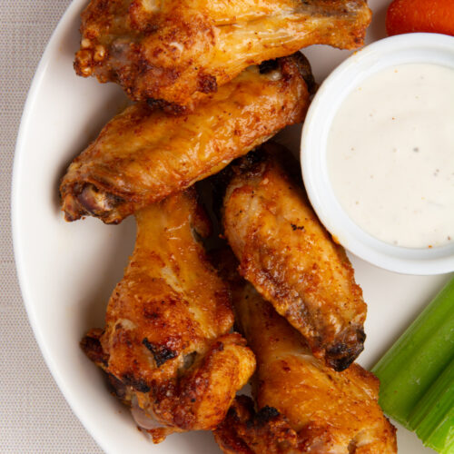 A plate of crispy chicken wings with carrot sticks, celery, and a side of ranch dressing.