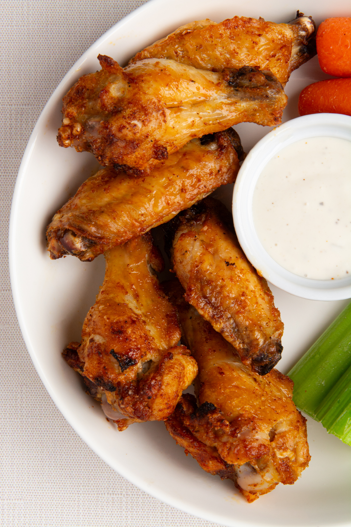 A plate of crispy chicken wings with carrot sticks, celery, and a side of ranch dressing.