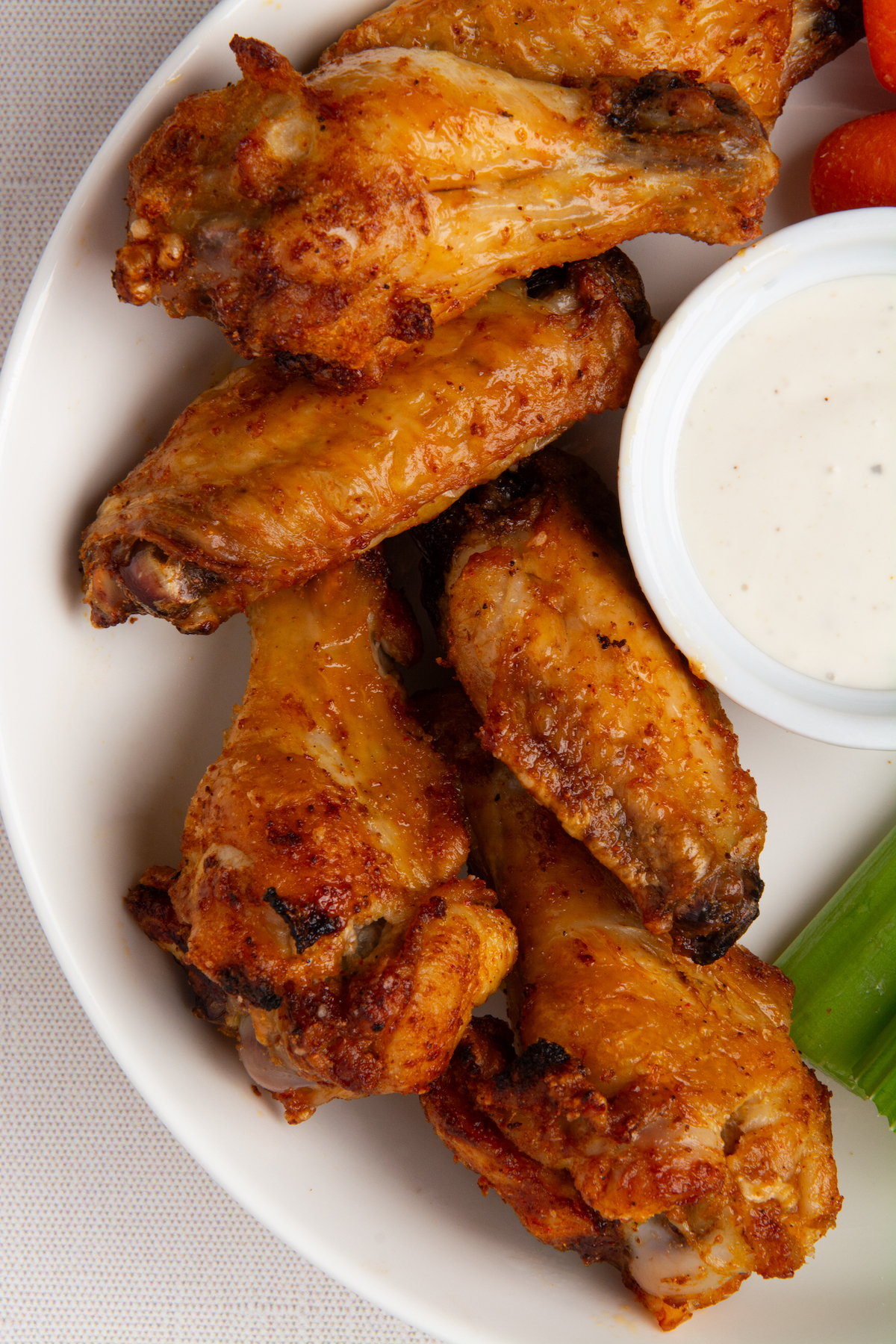 A plate of crispy chicken wings with carrot sticks, celery, and a side of ranch dressing.