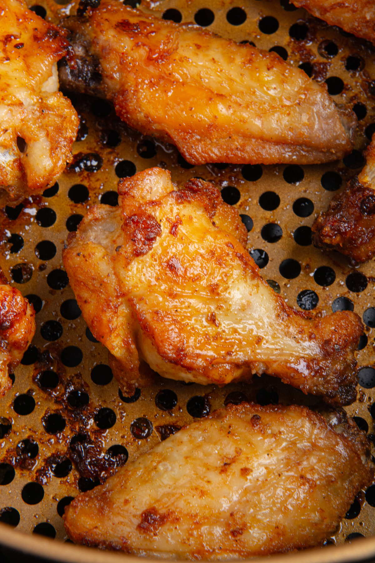 An air fryer basket with fully cooked, crispy chicken wings.