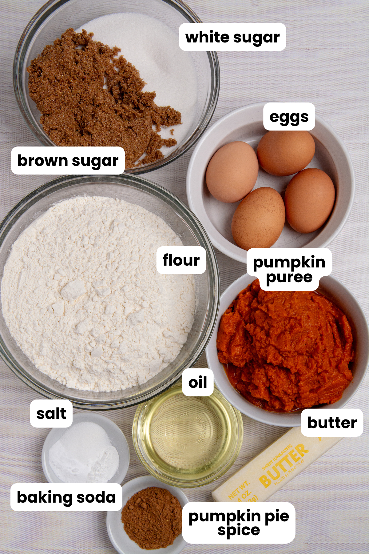 Ingredients for making pumpkin bread, white sugar, brown sugar, eggs, flour, pumpkin puree, oil, butter, pumpkin pie spice, baking soda, salt