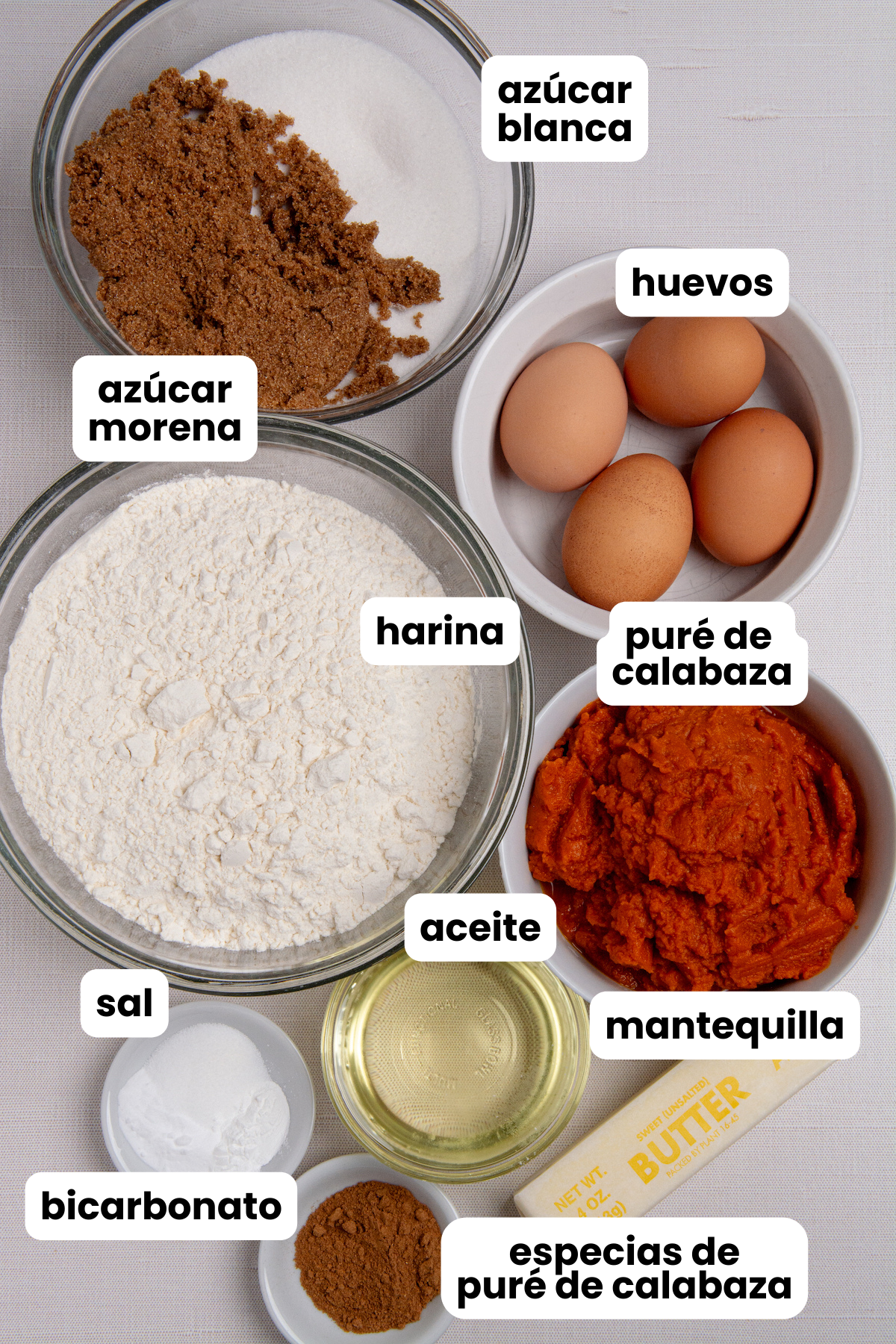 Ingredients for making pumpkin bread in Spanish, white sugar, brown sugar, eggs, flour, pumpkin puree, oil, butter, pumpkin pie spice, baking soda, salt