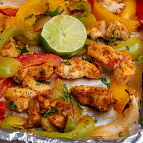 A baking sheet with cooked chicken fajitas with a squeezed lime wedge.