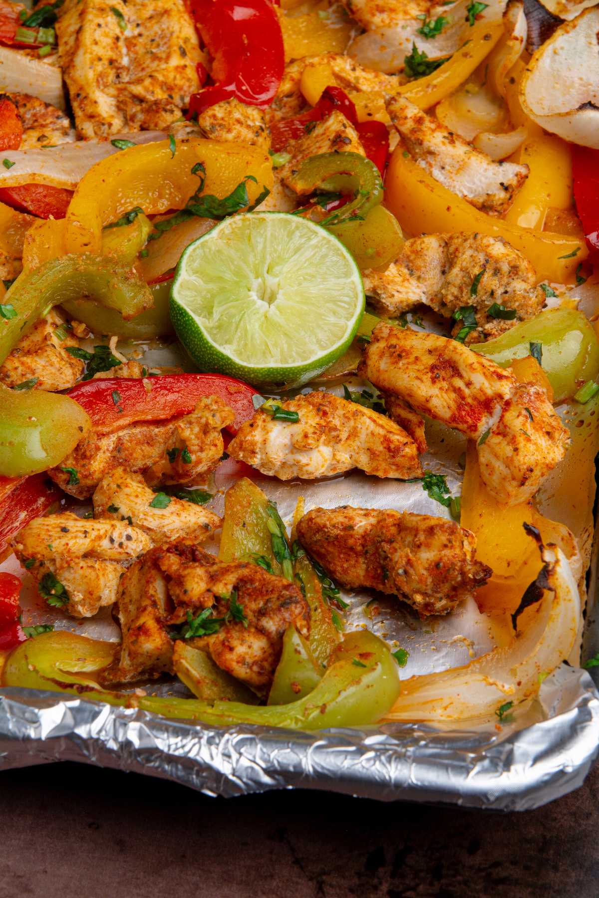 A baking sheet with cooked chicken fajitas with a squeezed lime wedge.