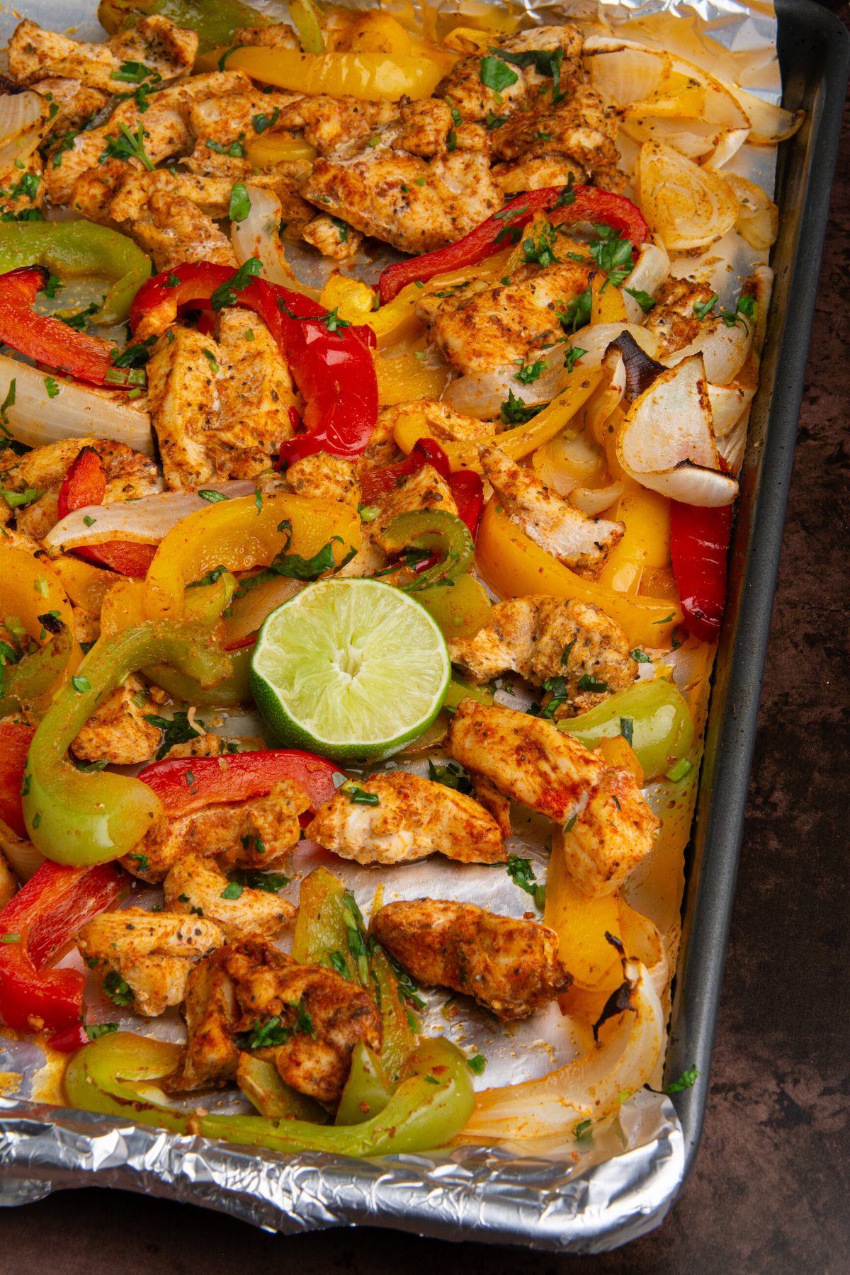 A baking sheet with cooked chicken fajitas with a squeezed lime wedge.