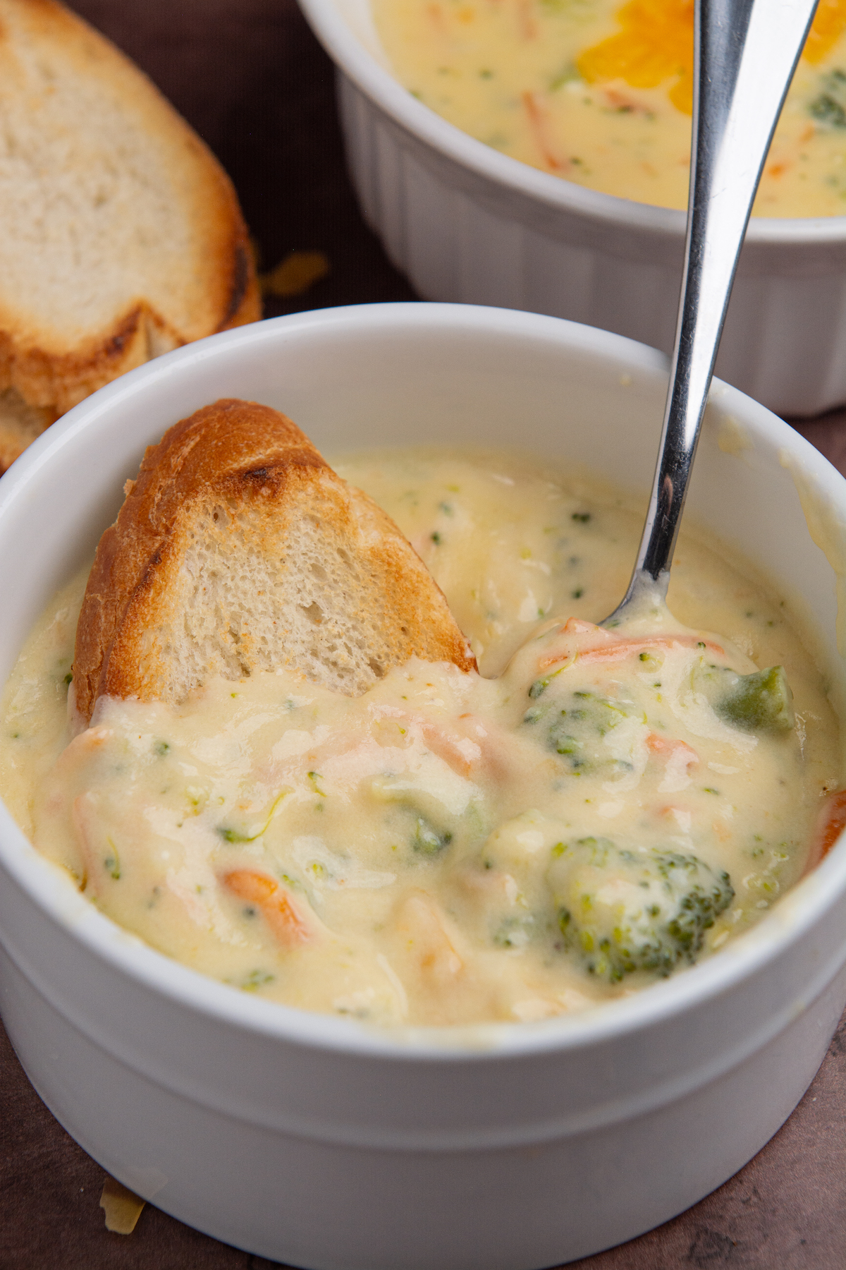 A bowl of broccoli cheddar soup with a piece of toasted bread and a spoon.