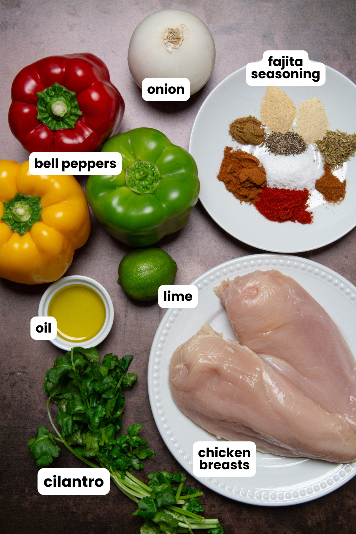 Ingredients for making sheet pan chicken fajitas, which include fajita seasoning, white onion, different colored bell peppers, lime, oil, cilantro, and chicken breasts.