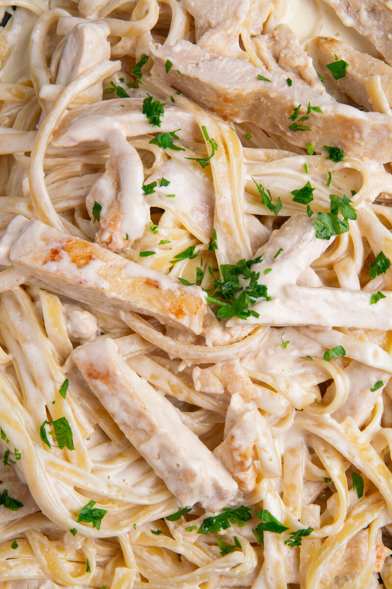 A large skillet with cooked Chicken Alfredo with fettuccine and a sprinkle of fresh chopped parsley.