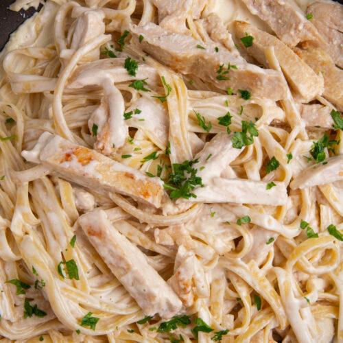 A large skillet with cooked Chicken Alfredo with fettuccine and a sprinkle of fresh chopped parsley.