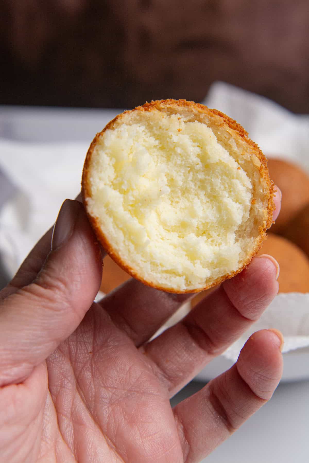 A hand holding a Colombian buñuelo cut in half showing a pillowy, soft center with a crispy, golden brown outer layer.