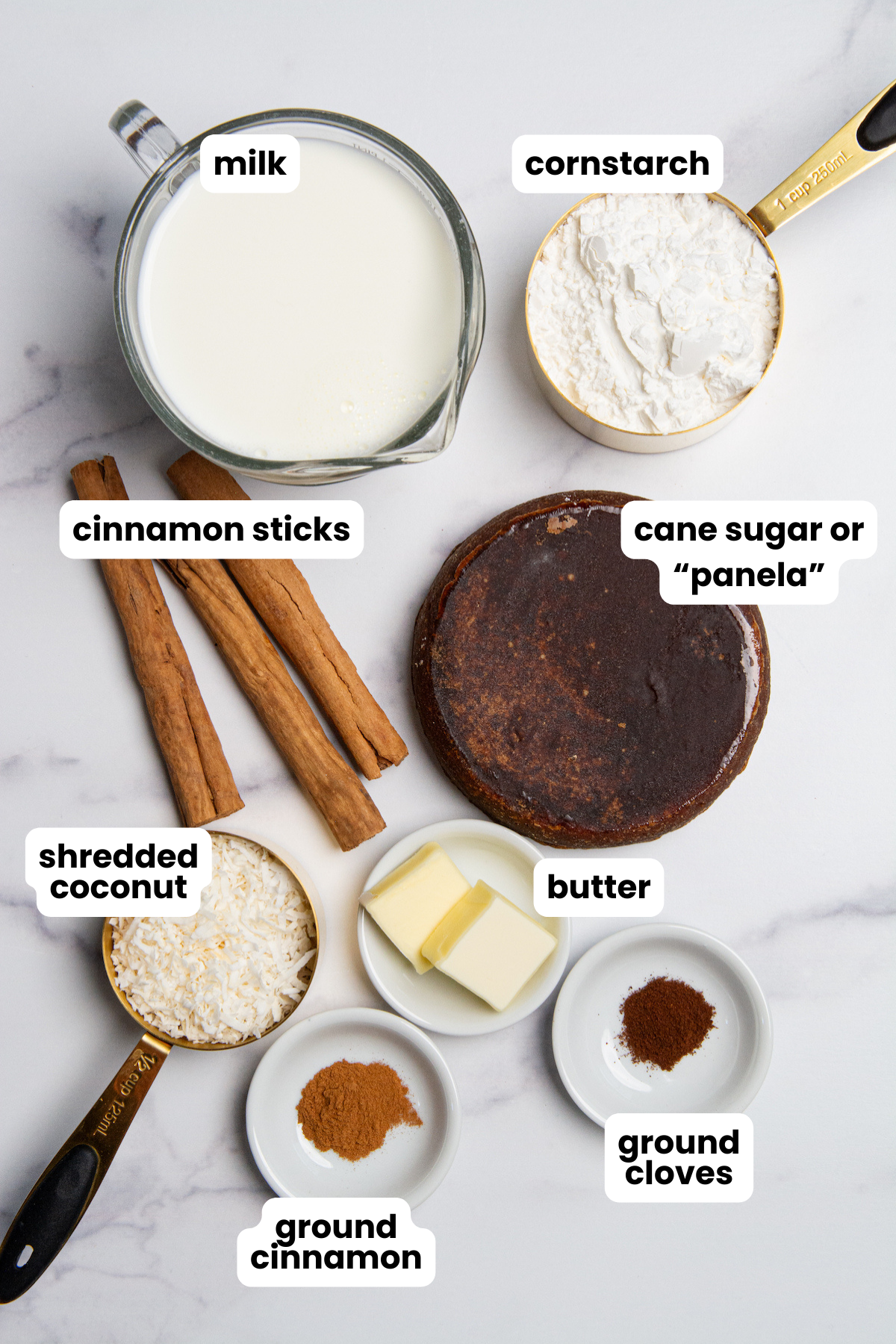 Ingredients for Colombian Natilla With Panela, milk, cornstarch, cinnamon sticks, cane sugar or panela, butter, ground cinnamon, ground cloves, and shredded coconut.