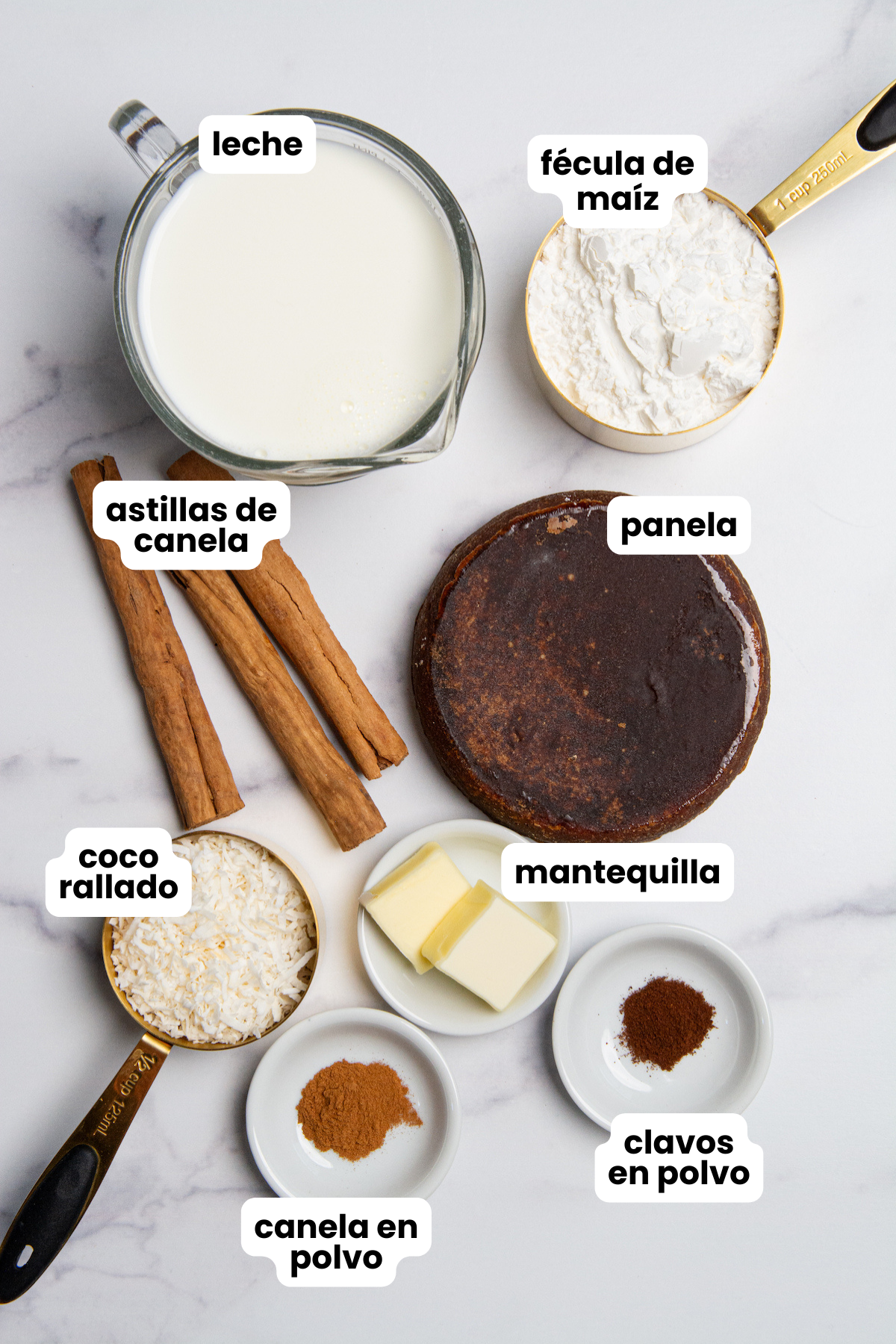 Ingredients for Colombian Natilla With Panela, milk, cornstarch, cinnamon sticks, cane sugar or panela, butter, ground cinnamon, ground cloves, and shredded coconut.