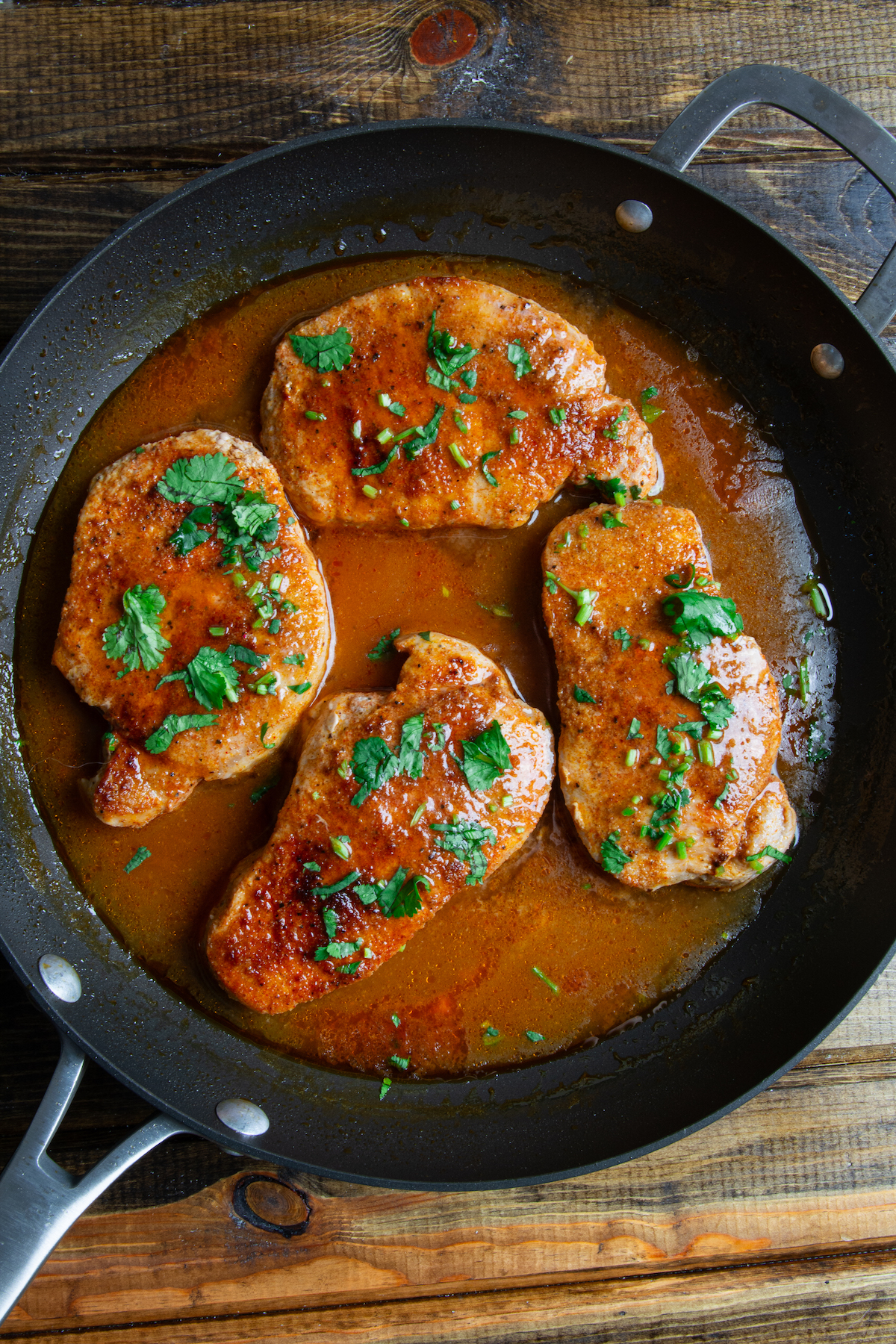 A skillet with pan seared boneless pork chops cooked in a delicious seasoned sauce and sprinkled with cilantro on top.