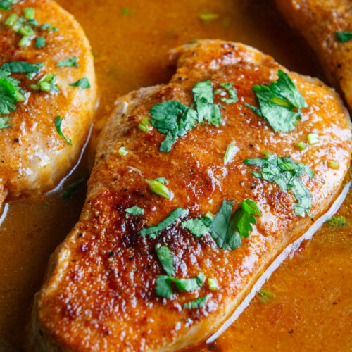 A skillet with pan seared boneless pork chops cooked in a delicious seasoned sauce and sprinkled with cilantro on top.